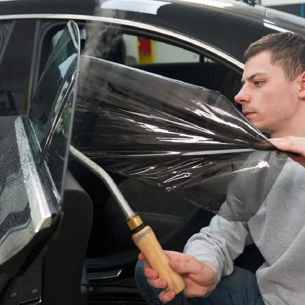 BlackFeather technician installing car window tint film using heat gun on a vehicle in Dubai