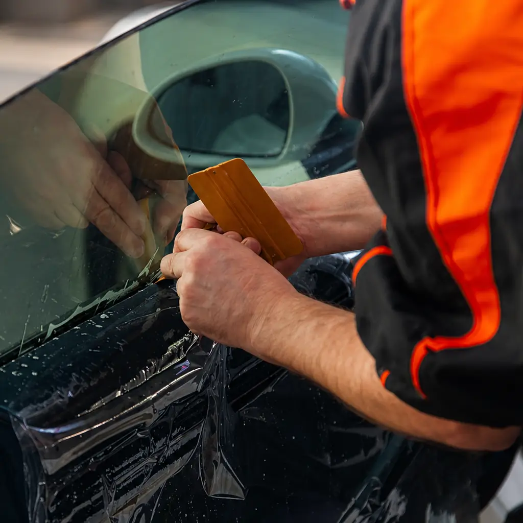 Technician applying black car tint film to vehicle window for privacy and heat reduction